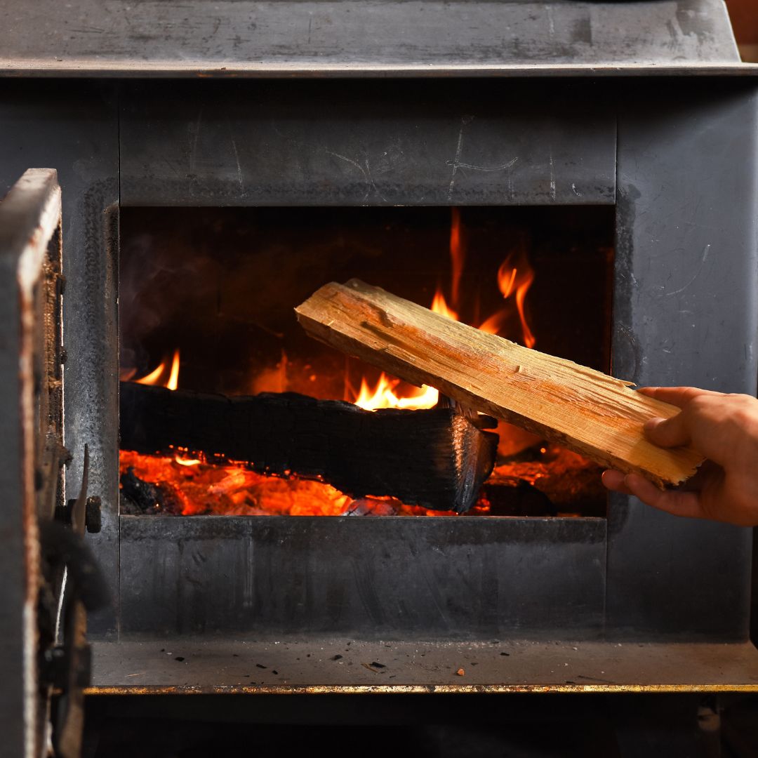 adding a piece of wood to a wood-burning stove